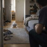 Robot doméstico en un salón real mientras una persona y un gato lo observan sin interactuar